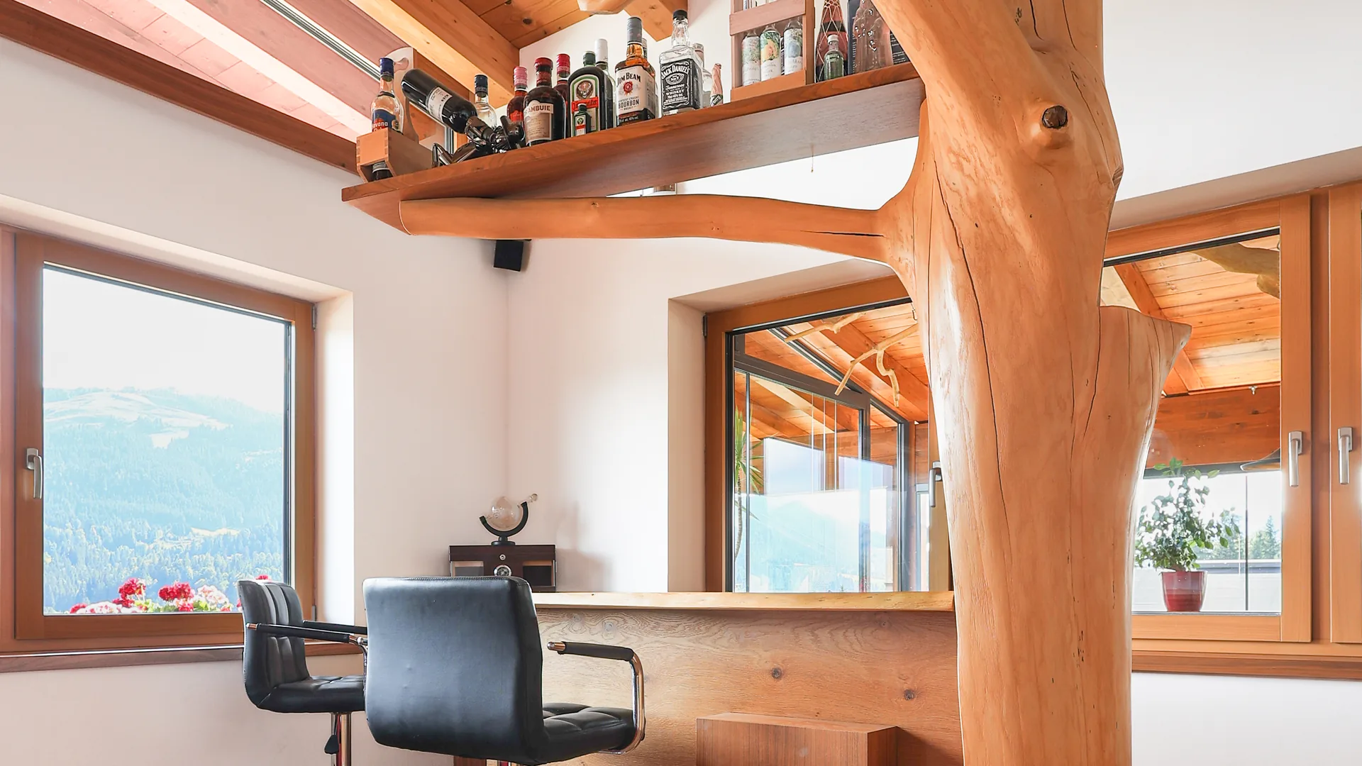Die außergewöhnliche natürliche Baumkonstruktion im Wohnzimmer mit Bar und Bergblick — das Herzstück des FALKENSITZ