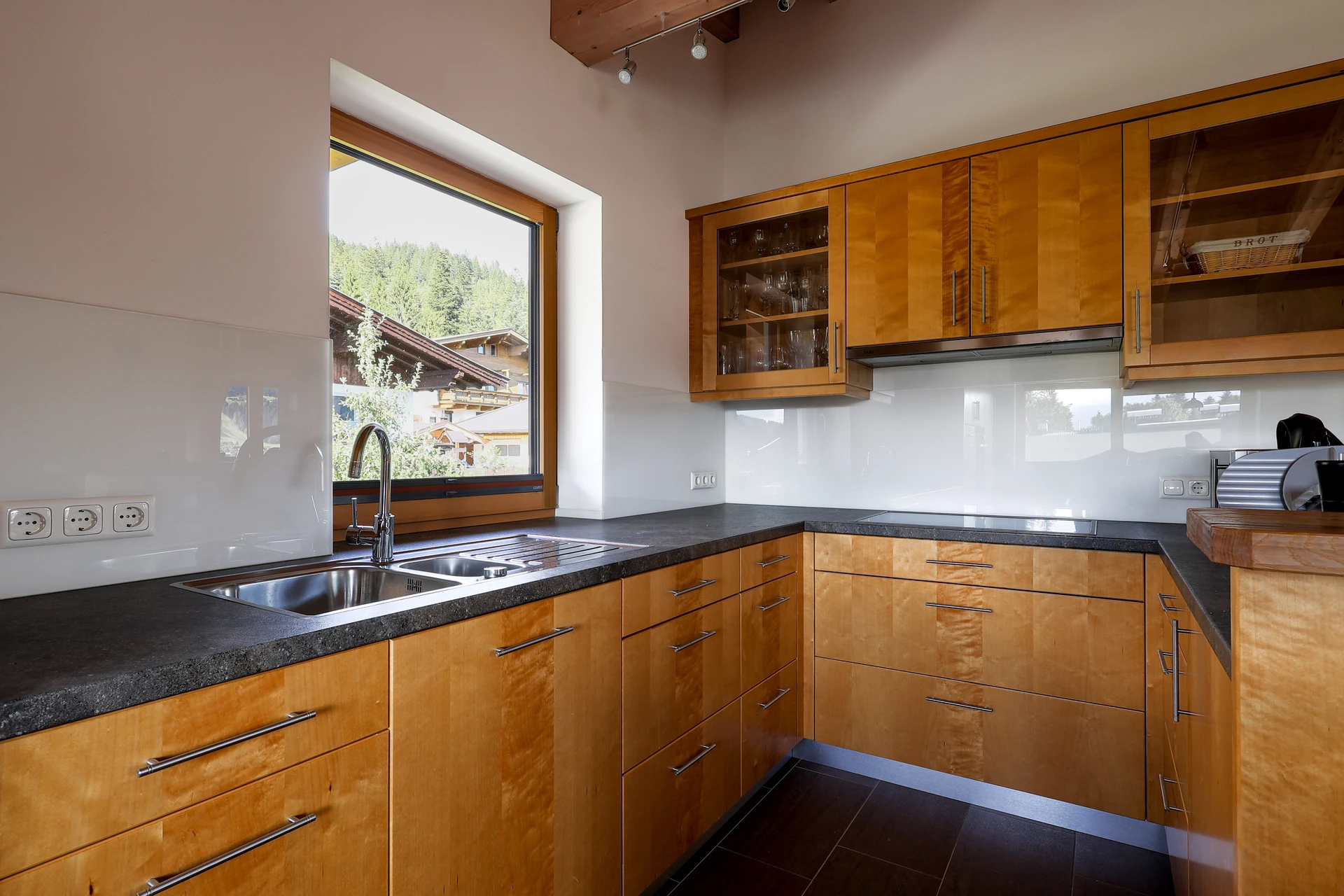 Tischlerküche mit Birke-Maser-Fronten, dunkler Granit-Arbeitsplatte und Glasoberschränken im FALKENSITZ Apartment Ellmau