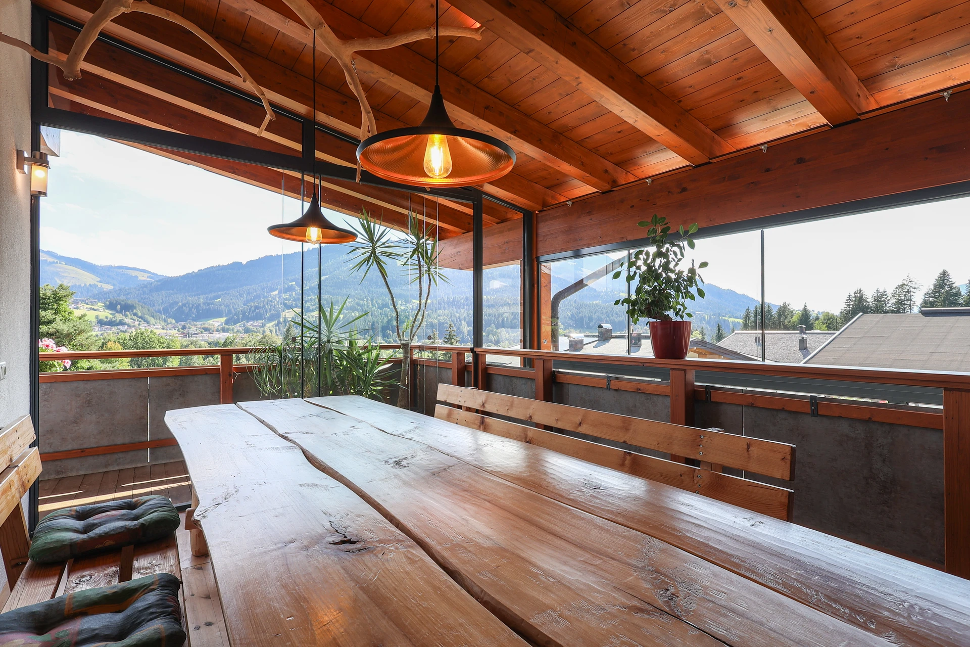 Verglaste Panorama-Terrasse im FALKENSITZ mit massivem Holztisch, Hängelampen und freiem Blick auf den Wilden Kaiser